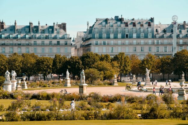 Jardin parisien ensoleillé avec statues et passants.