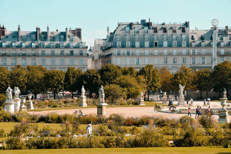 Jardin parisien ensoleillé avec statues et passants.