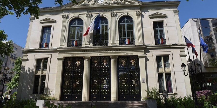Mairie française avec drapeaux tricolores et arbres verts.
