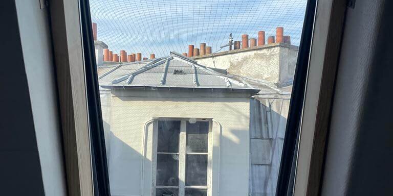 Vue sur toits par fenêtre mansardée et ciel bleu.